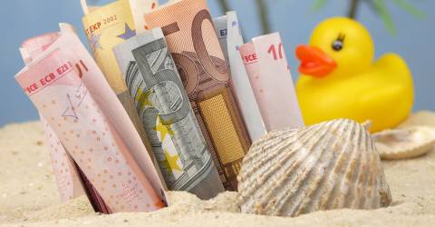 Vakantiegeld; briefgeld op een strand met palmbomen op de achtergrond een schelp en een badeend